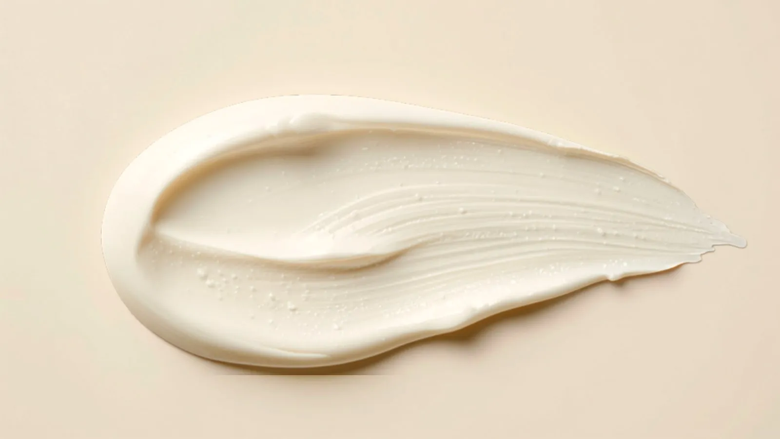 Texturprov av en vit, matt fuktkräm utstruken på varmbeige bakgrund